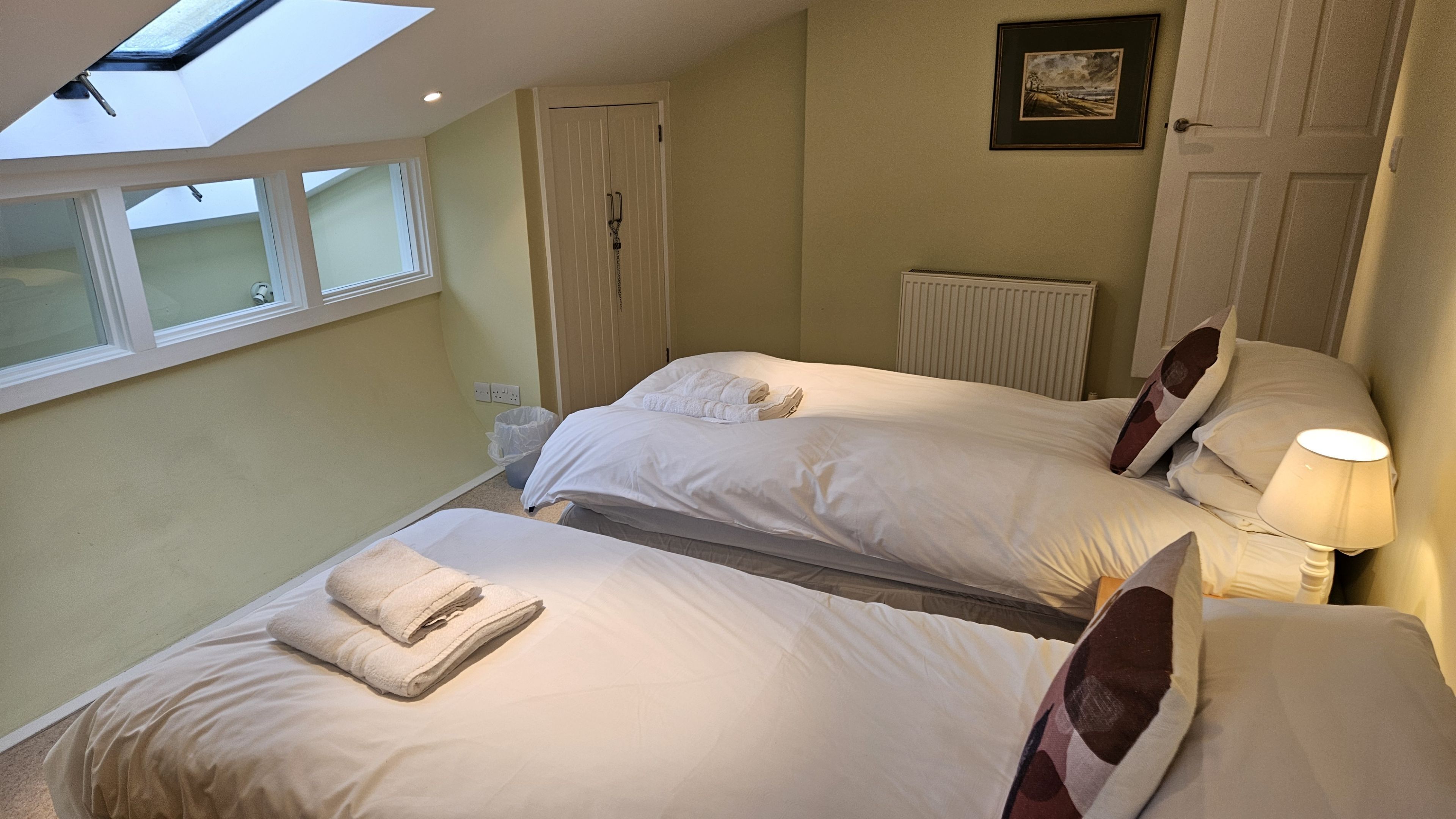 A hotel room with two beds, a skylight, a radiator, and a framed picture on the wall.