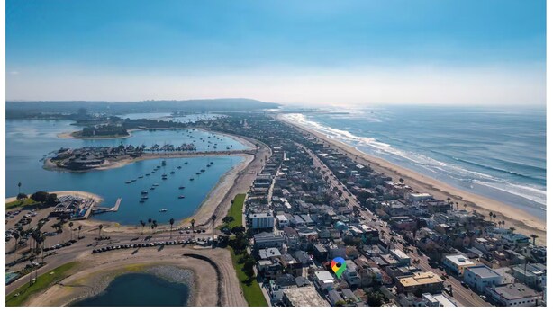 Vista aérea de una zona costera con un puerto deportivo, playa y edificios muy juntos.