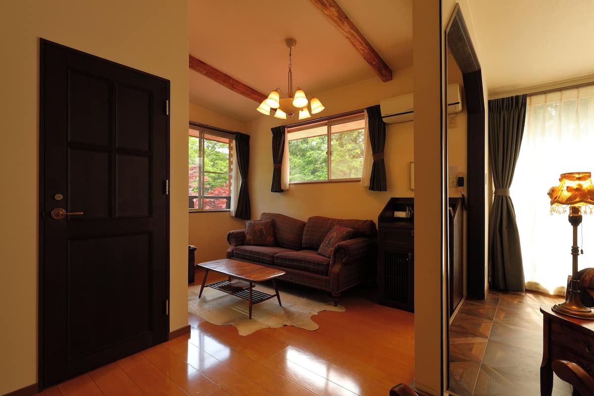 A cozy living room with a dark wooden door, a brown sofa, a small coffee table, and a ceiling light fixture.