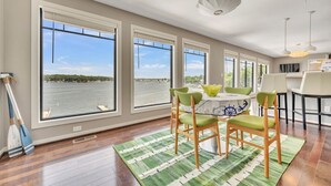 A dining area with large windows overlooking a body of water, wooden flooring, and a green rug. - Penthouse Suite, gorgeous West Lake Okoboji views, 1 BDRM above shopping center (Arnolds Park)