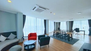 A modern hotel room with a wooden floor, a sofa, a red chair, a dining table with chairs, and large windows with curtains. - BB hotel Savannakhet Laos (Savannakhet)