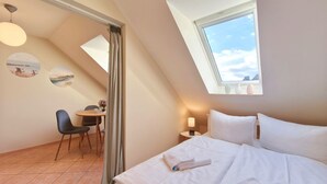 A bedroom with a bed, a desk, and a chair. There is a skylight above the bed and a window on the right.