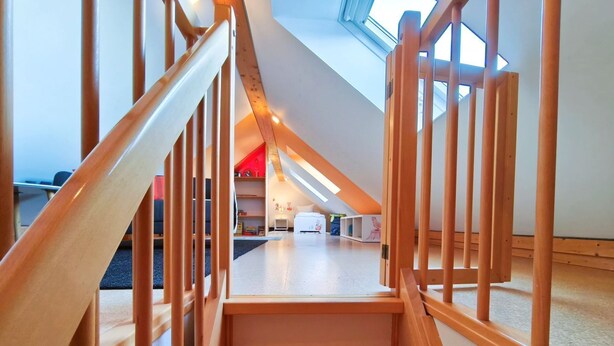 A wooden staircase leading to a loft bedroom with a skylight.