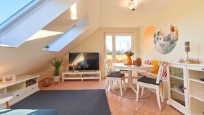A modern living room with a TV, dining table, chairs, and a skylight.