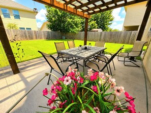 An outdoor patio with a table and chairs, surrounded by a wooden pergola.