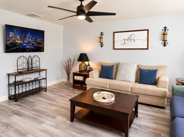 Una sala de estar con sofá, mesa de centro, televisor, objetos decorativos y una pintura de un paisaje urbano.