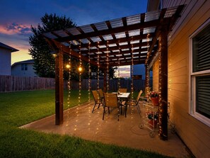 Un porche cubierto con luces colgantes, una mesa, sillas y una planta en maceta.