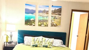 Une chambre à coucher avec un lit, un ventilateur de plafond, une table de chevet avec une lampe et trois tableaux encadrés accrochés au mur.