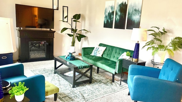 Un salon avec un canapé vert, des fauteuils bleus, une table basse et une cheminée.