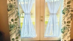 Une double porte ornée de rideaux légers et d’un motif floral, qui donne sur un espace extérieur.