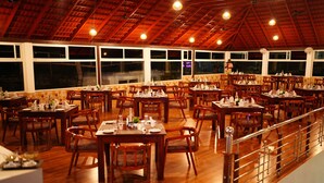 Een restaurant met meerdere houten tafels en stoelen, grote ramen en een houten plafond.