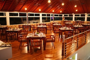 Un restaurante con varias mesas y sillas de madera, ventanas amplias y techo de madera.