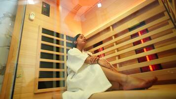 A person in a white robe sitting on a wooden bench in a room with a wooden slat wall and a control panel on the wall.