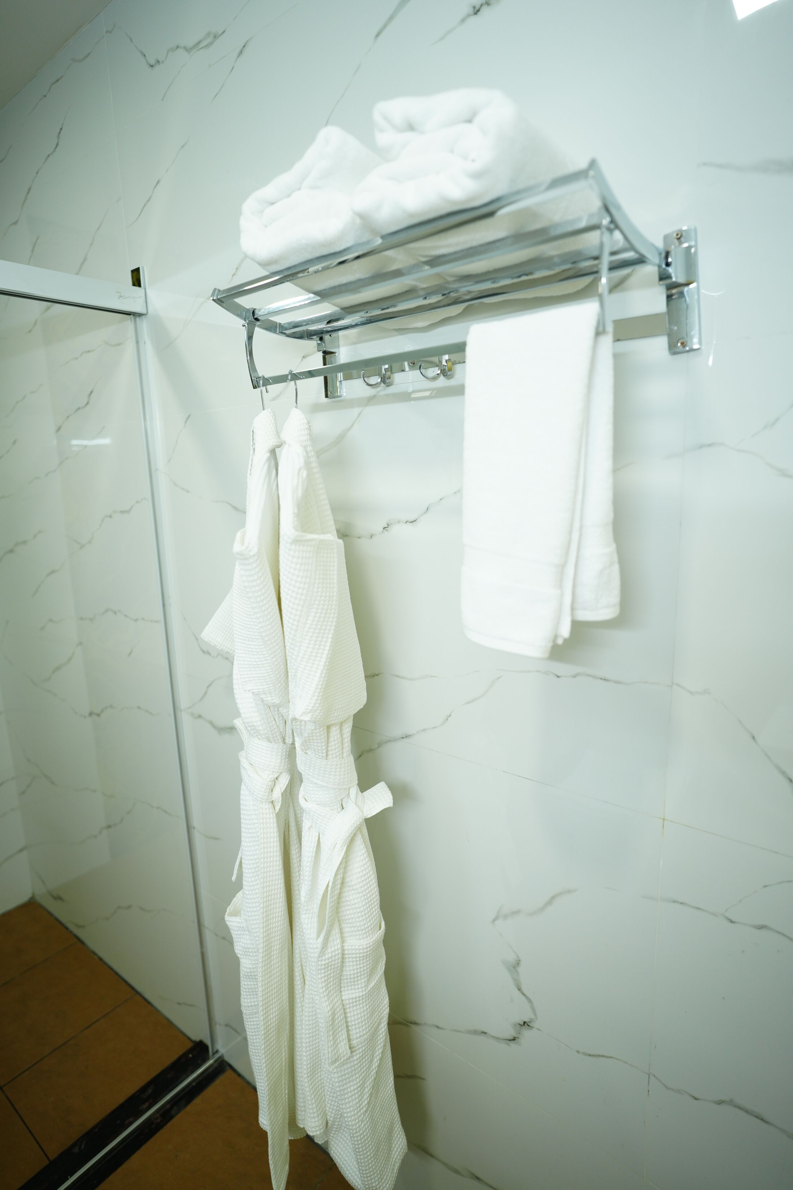 Un baño con pared de mármol, puerta de ducha de vidrio y un perchero con toallas dobladas.