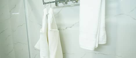 Un baño con pared de mármol, puerta de ducha de vidrio y un perchero con toallas dobladas.