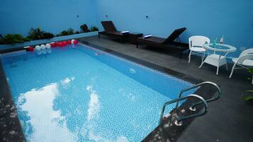 Ein Swimmingpool mit Liegestühlen und einem Tisch, umgeben von einer blauen Wand.