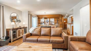 Una sala moderna con un sofá de cuero marrón, una mesa de centro de madera y un comedor con un armario de madera y una lámpara colgante.