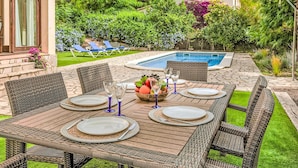 Une terrasse avec une piscine, des meubles en osier et une table dressée pour le repas.