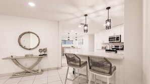 Une cuisine moderne avec des meubles blancs, un îlot central doté de tabourets et des luminaires suspendus.