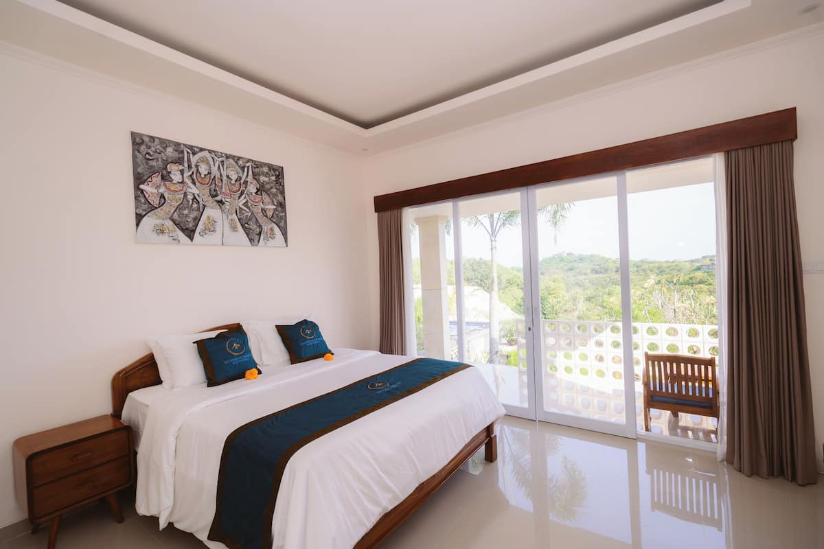 Une chambre d’hôtel avec un grand lit, une table de chevet, un tableau au mur et un balcon avec vue.