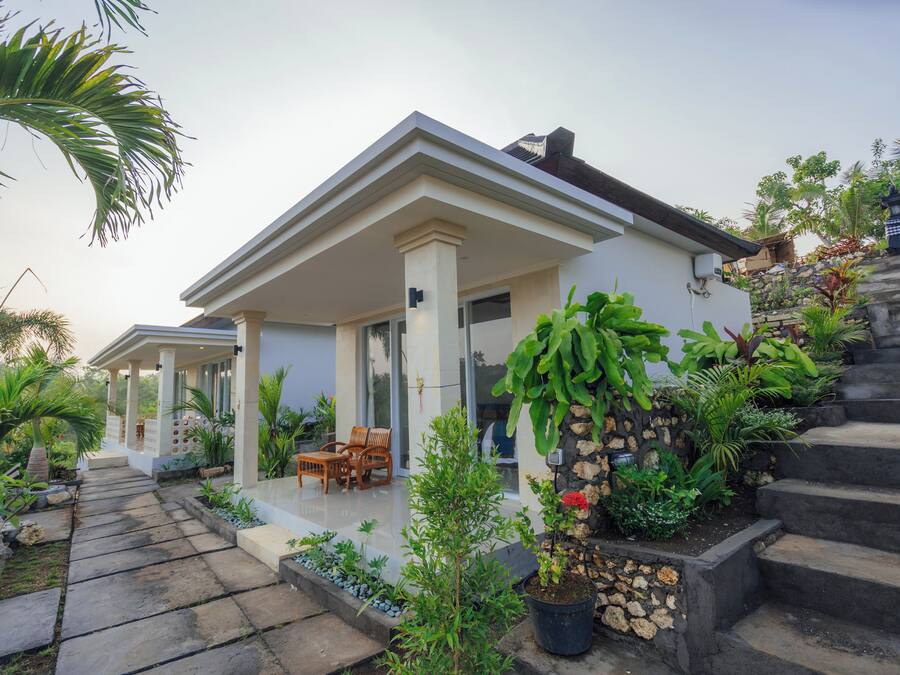 Una casa moderna con porche cubierto, escalones de piedra y abundante vegetación.