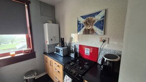 Une cuisine équipée d’une cuisinière à gaz, d’un four à micro-ondes, d’un chauffe-eau et d’une fenêtre donnant sur l’extérieur.