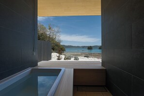 Un baño moderno con una bañera grande, una terraza de madera y vistas a una playa y montañas.