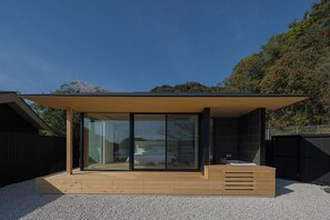 Un área de spa moderna al aire libre con terraza de madera, cerramiento de vidrio y un ventanal grande.