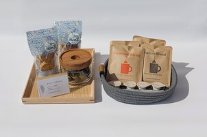 Uma bandeja de madeira com um pote de vidro e uma colher de madeira, duas embalagens transparentes com estampas florais azuis, e duas sacolas de papel pardo rotuladas "Toyotomi Blend".
