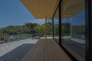 Una terraza de madera con barandilla de vidrio que da a un jardín ajardinado con árboles y un cuerpo de agua.