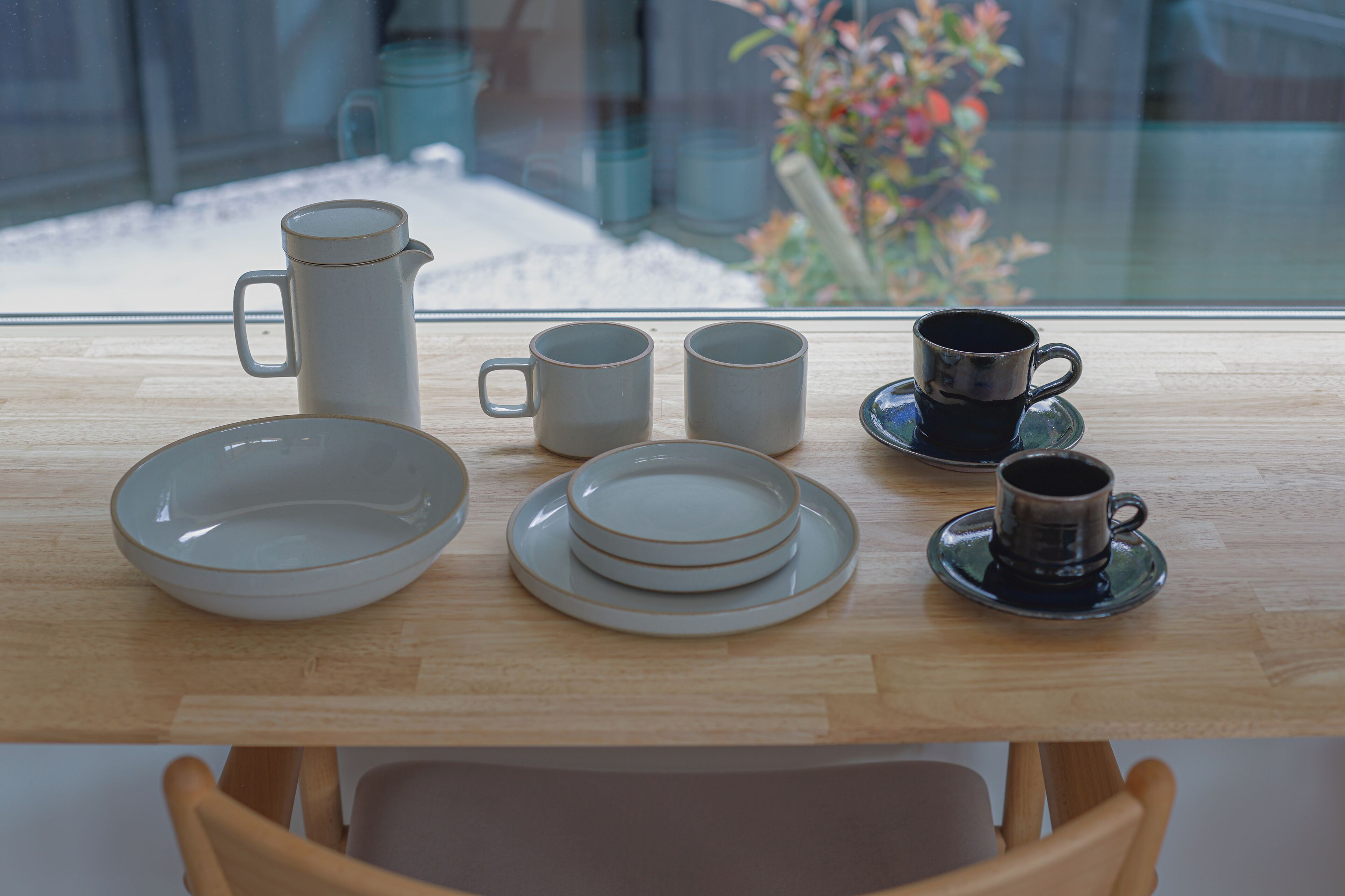 A wooden table with a pitcher, three cups, a saucer, and a bowl.