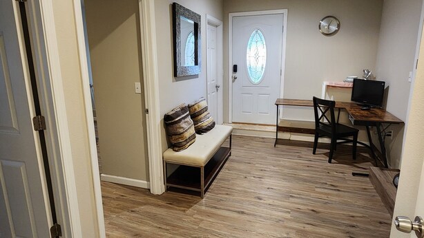 A hallway with a bench, a door with a stained glass window, and a desk with a computer.