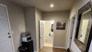 A hallway with wooden flooring, a bench, a trash can, and a microwave on a stand.