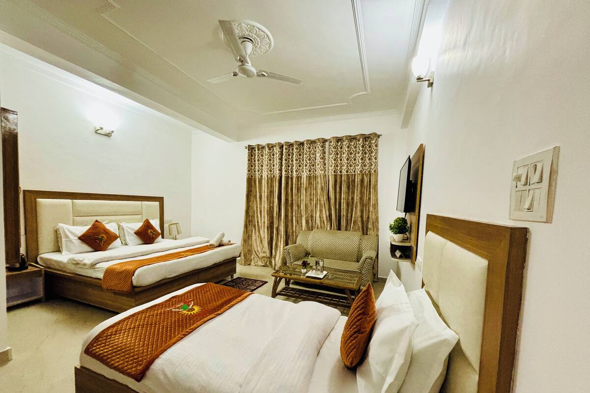A hotel room with two beds, a sofa, a ceiling fan, and a TV mounted on the wall.