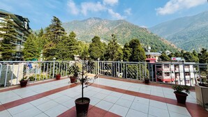 A terrace with potted plants, a view of mountains, and a hotel sign. - kumar residency Mcleodganj (Dharamshala)