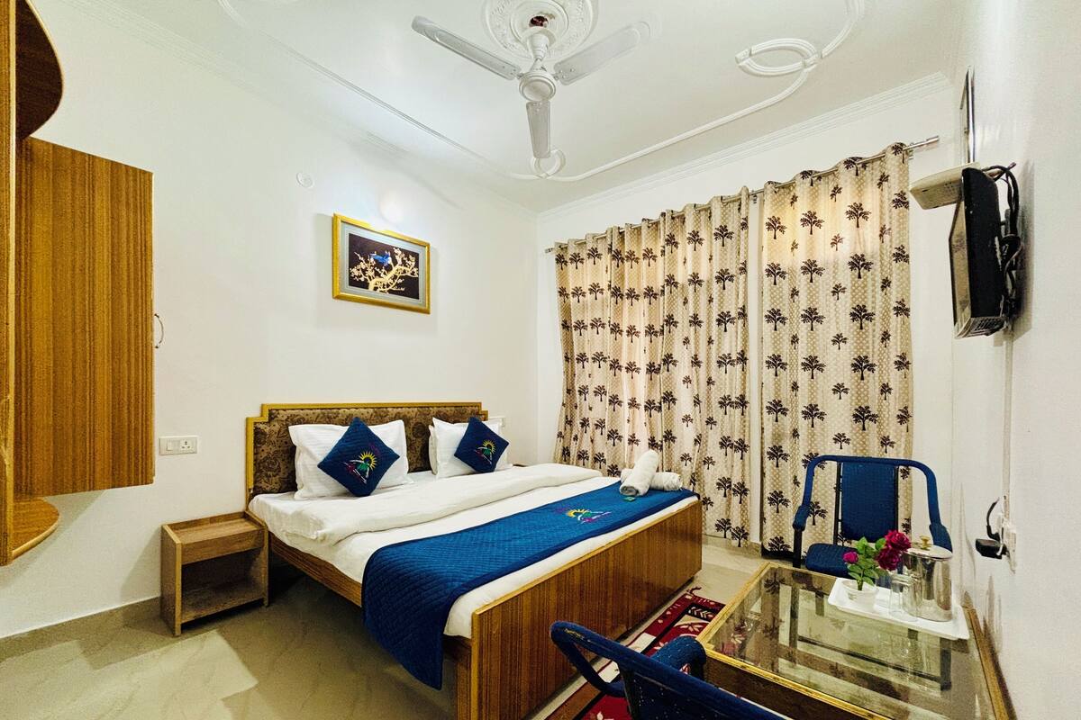 A bedroom with a bed, a nightstand, a chair, a table, a ceiling fan, and curtains.