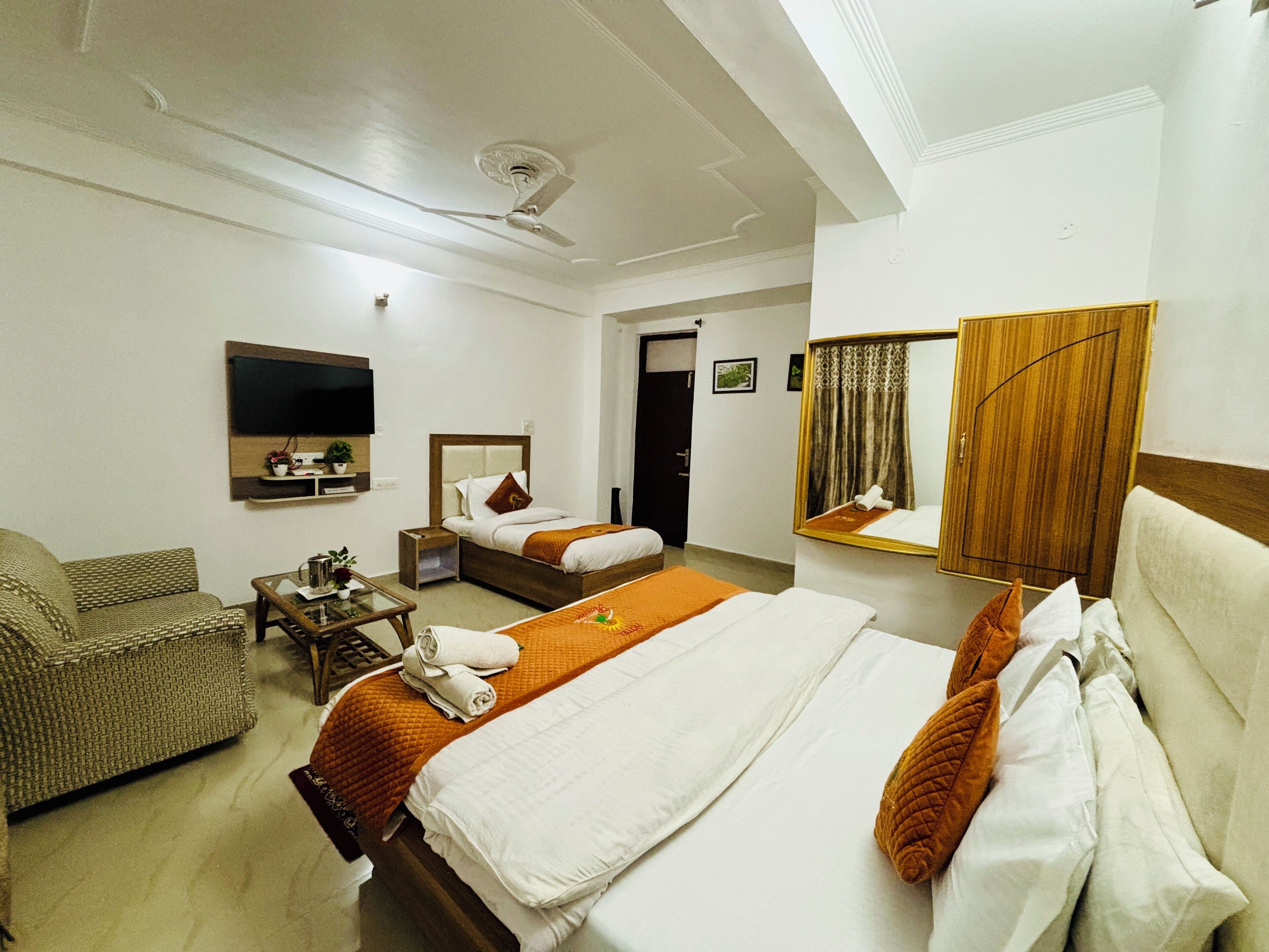 Une chambre d’hôtel équipée d’un lit, d’un canapé, d’une télévision, d’un miroir et d’un ventilateur de plafond.