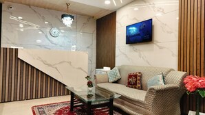 A modern living room with a sofa, a glass coffee table, a clock, a TV, and a wooden panel wall. - kumar residency Mcleodganj (Dharamshala)