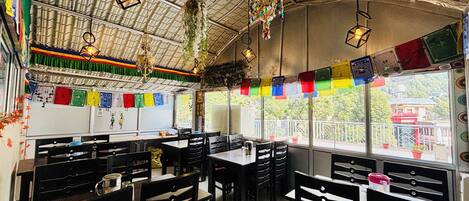 A restaurant with a high ceiling, hanging lanterns, and colorful prayer flags. Tables and chairs are arranged for dining.
