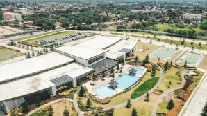 Vista aérea de un campus con un edificio grande, estacionamiento, piscina y zonas ajardinadas.