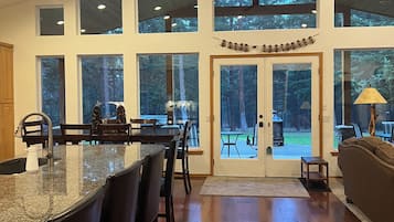 A spacious kitchen with a large island, multiple windows, and a view of the surrounding forest.