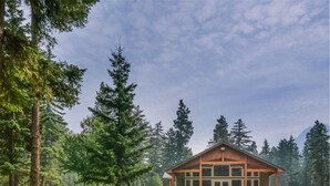 Un chalet doté d’une grande véranda, entouré de grands arbres et offrant une vue sur un ciel dégagé.