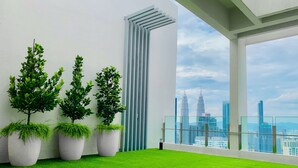 A balcony with artificial grass, three potted plants, and a view of the city skyline including the Petronas Towers. - Comfort Suite At Agile  (Kuala Lumpur)