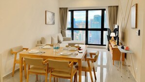 A modern dining area with a large table set for four, a sofa, and a TV stand with a lamp. - Comfort Suite At Agile  (Kuala Lumpur)