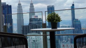 A balcony with a potted plant, overlooking a cityscape with tall buildings, including a prominent tower with a spire. - Comfort Suite At Agile  (Kuala Lumpur)