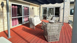 Ein überdachter Patio-Bereich mit Korbmöbeln, rotem Boden und großen Schiebeglastüren, die zu einem Innenraum führen.