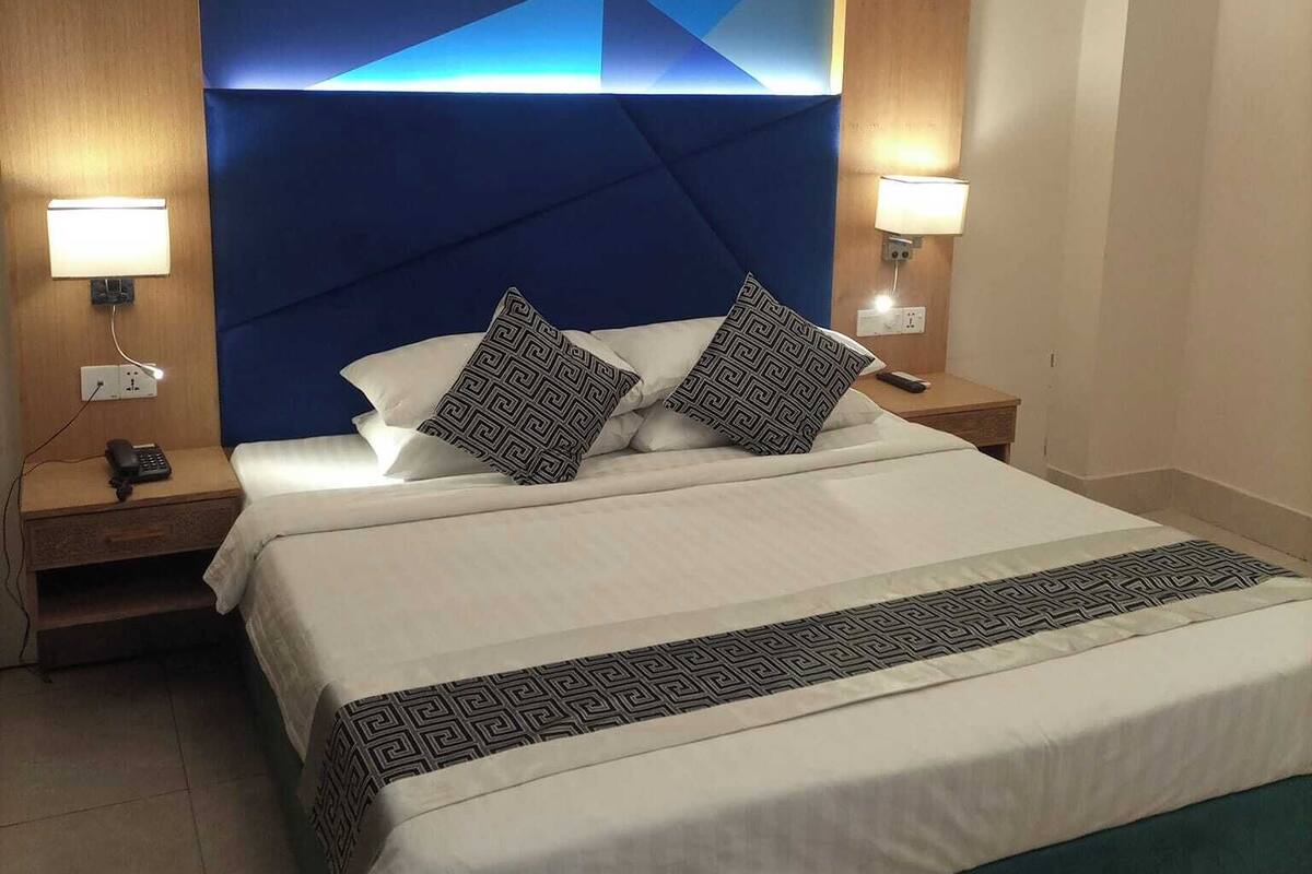 A modern hotel room with a large bed, geometric wall design, and two bedside lamps.