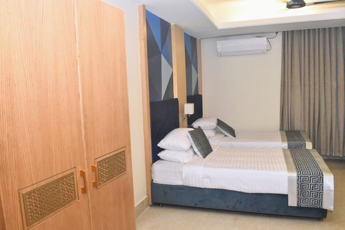 A hotel room with two beds, a wooden wardrobe, a geometric-patterned headboard, and a ceiling light.