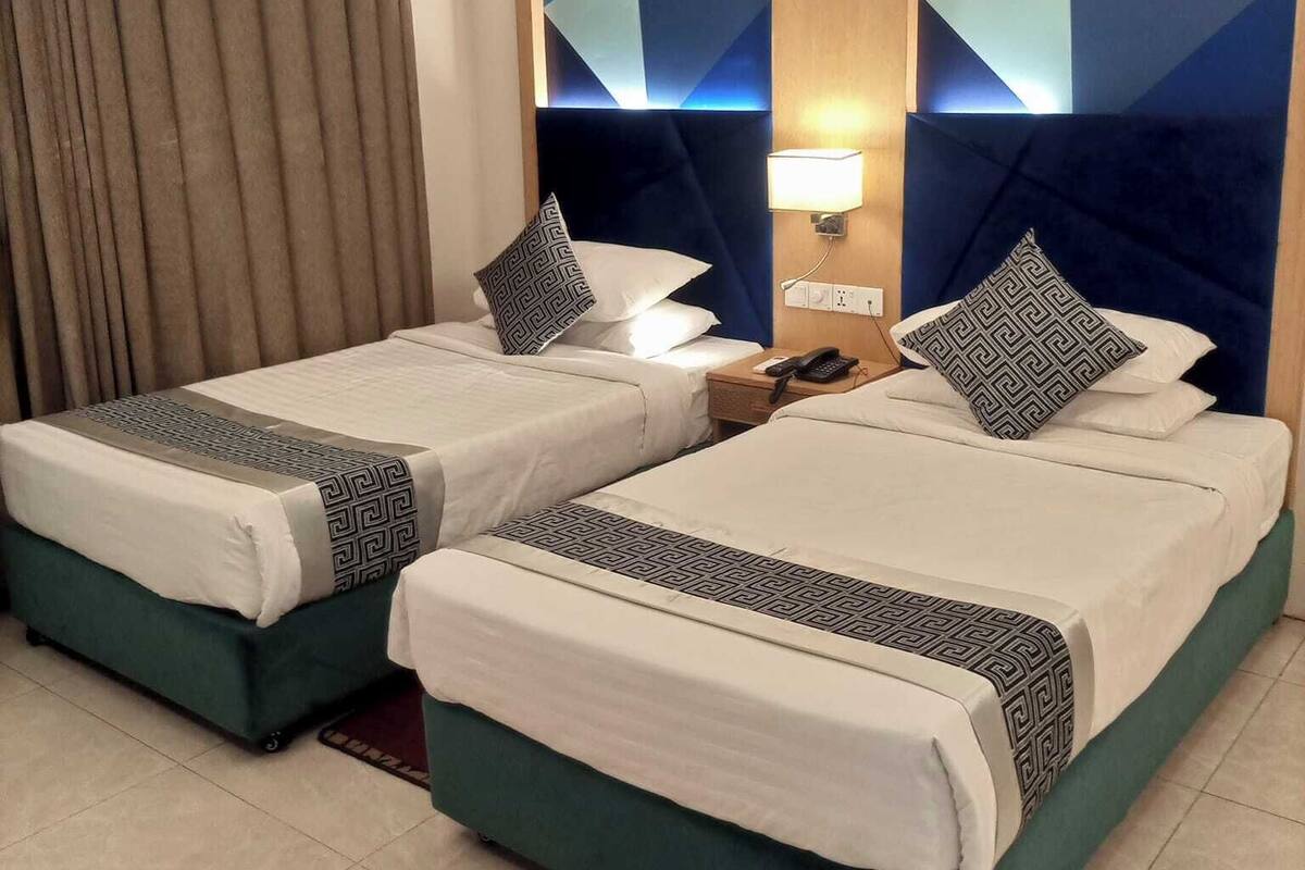 A hotel room with two beds, a nightstand, a lamp, and a geometric wall design.
