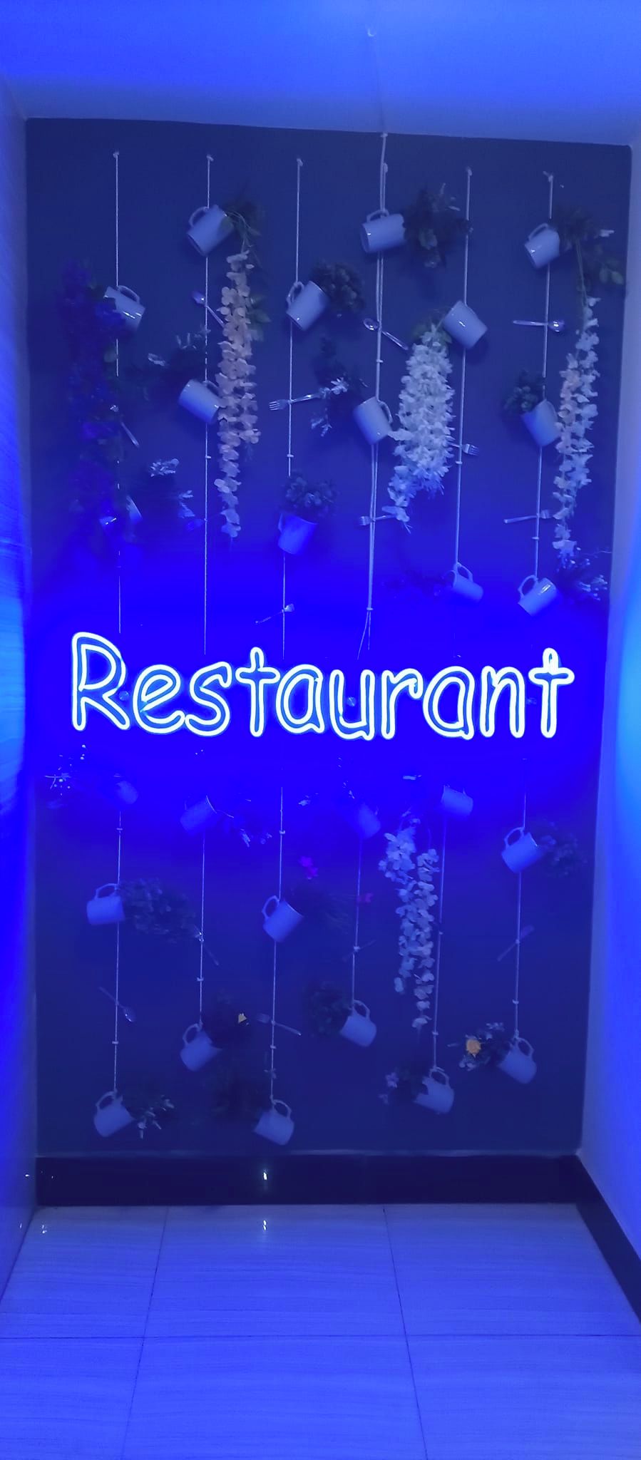 A wall with a neon sign reading "Restaurant" and hanging planters with white flowers.